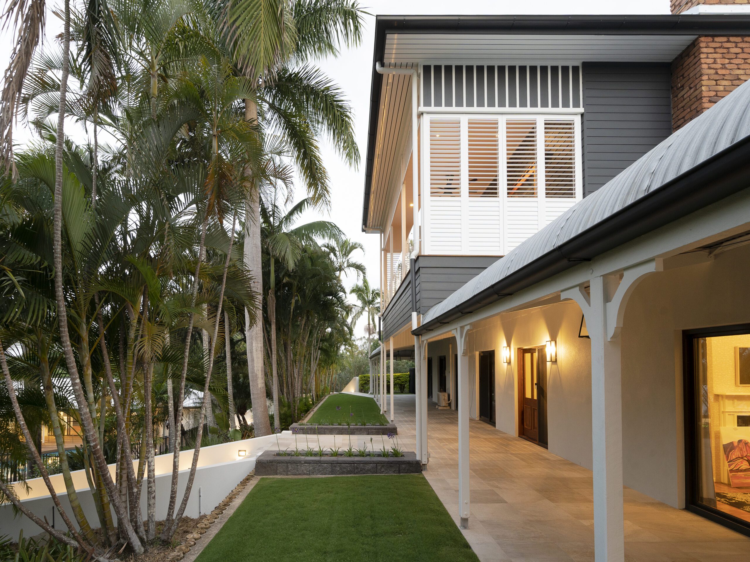 Brookfield renovation side perspective showing elevated Queenslander-style home with landscaped gardens, tiled verandah, and timber detailing.