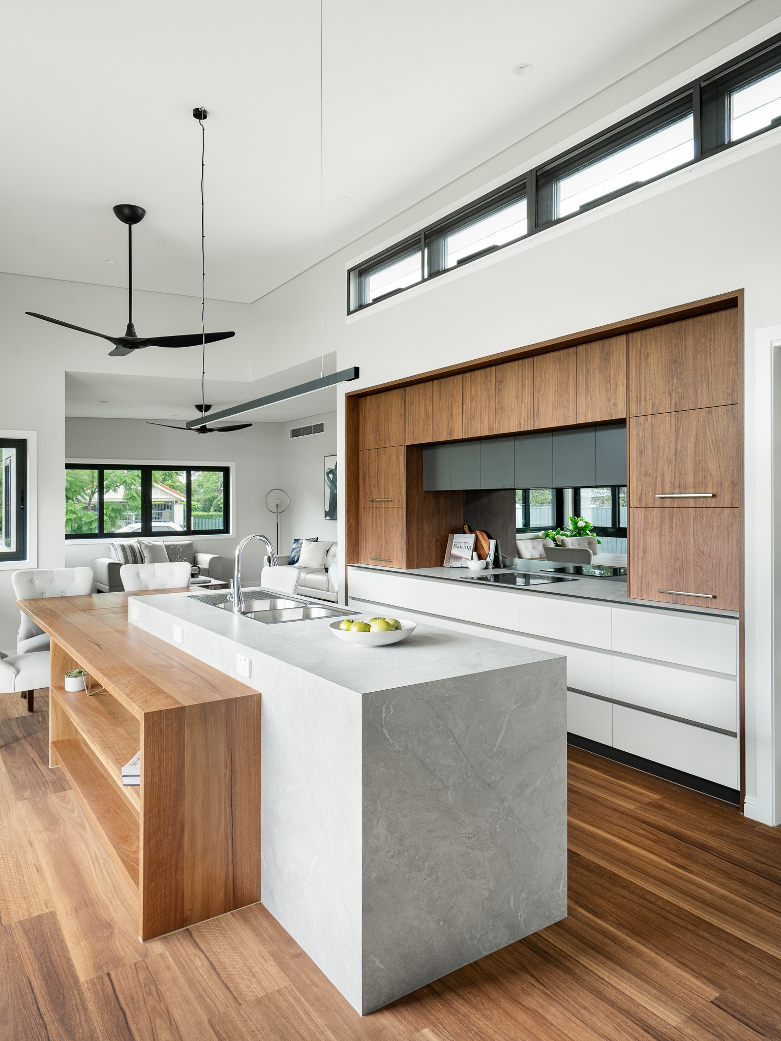 Modern open-plan kitchen and dining space with timber flooring, large island bench, overhead fan, and windows providing natural light.