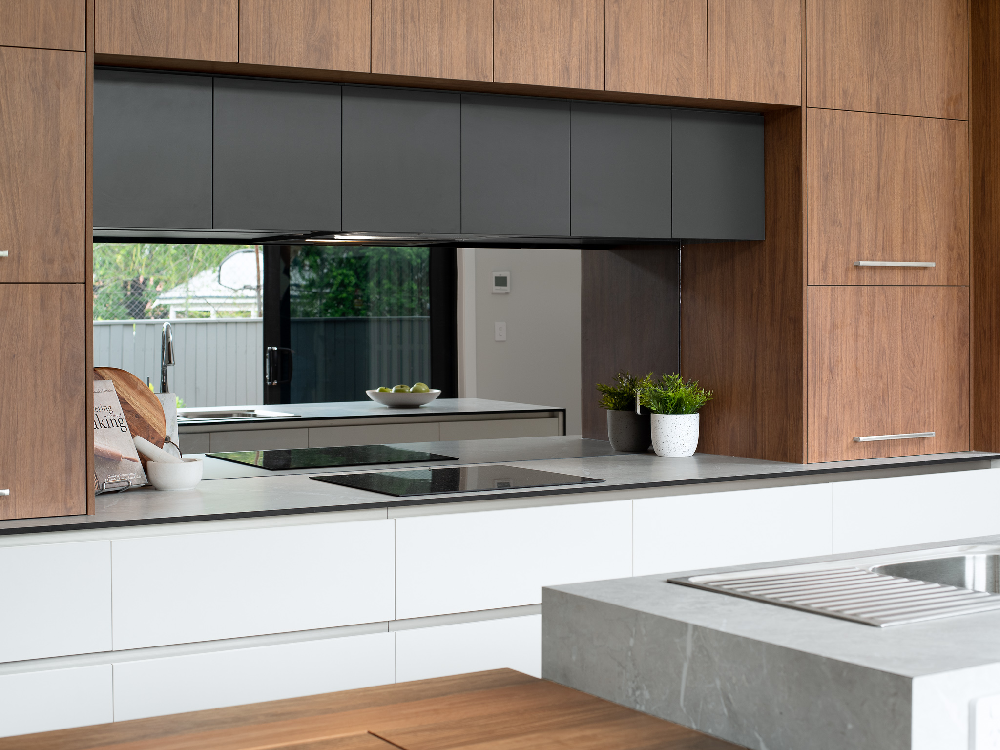 Contemporary kitchen with timber cabinetry, integrated cooktop and rangehood, concrete benchtop, black-framed window splashback, and an island with sink — designed with energy efficiency and natural ventilation in mind.