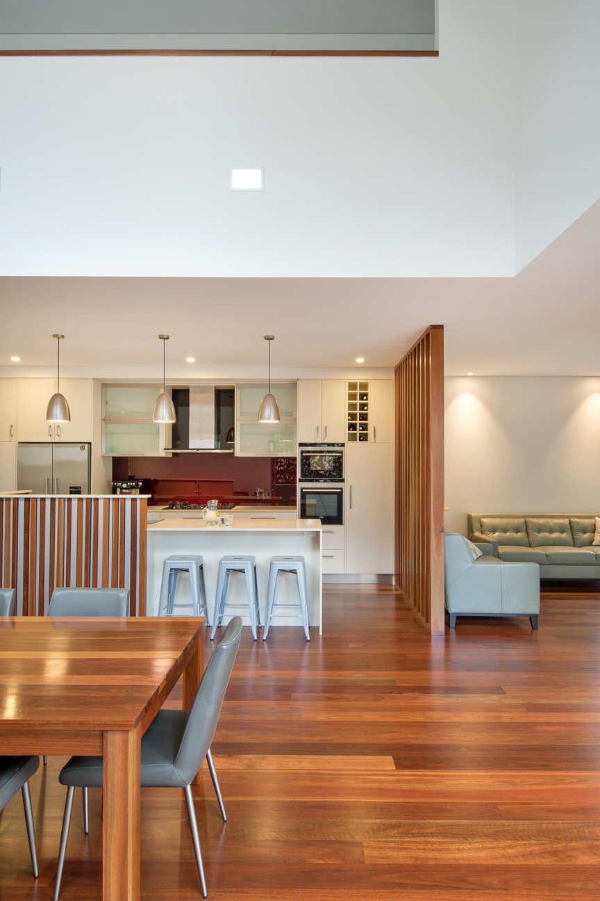 Warm and cohesive open-plan kitchen, dining, and living space in a Brisbane home, featuring timber floors, vertical screening, and integrated lighting for a calm, functional layout.