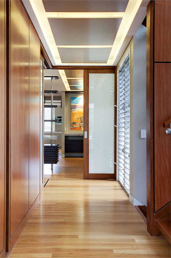 Interior hallway of a contemporary home featuring warm timber flooring, integrated cabinetry, and recessed ceiling lighting. A framed artwork draws the eye through the space, creating a sense of flow and alignment between architecture and interior design.